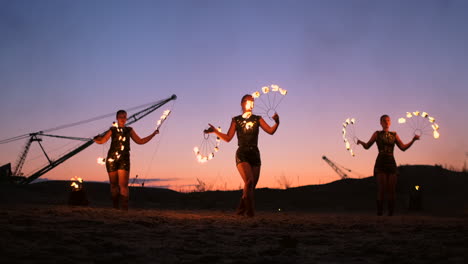 Feuershow:-Drei-Frauen-In-Ihren-Händen-Drehen-Brennende-Speere-Und-Fächer-Im-Sand-Mit-Einem-Mann-Mit-Zwei-Flammenwerfern-In-Zeitlupe